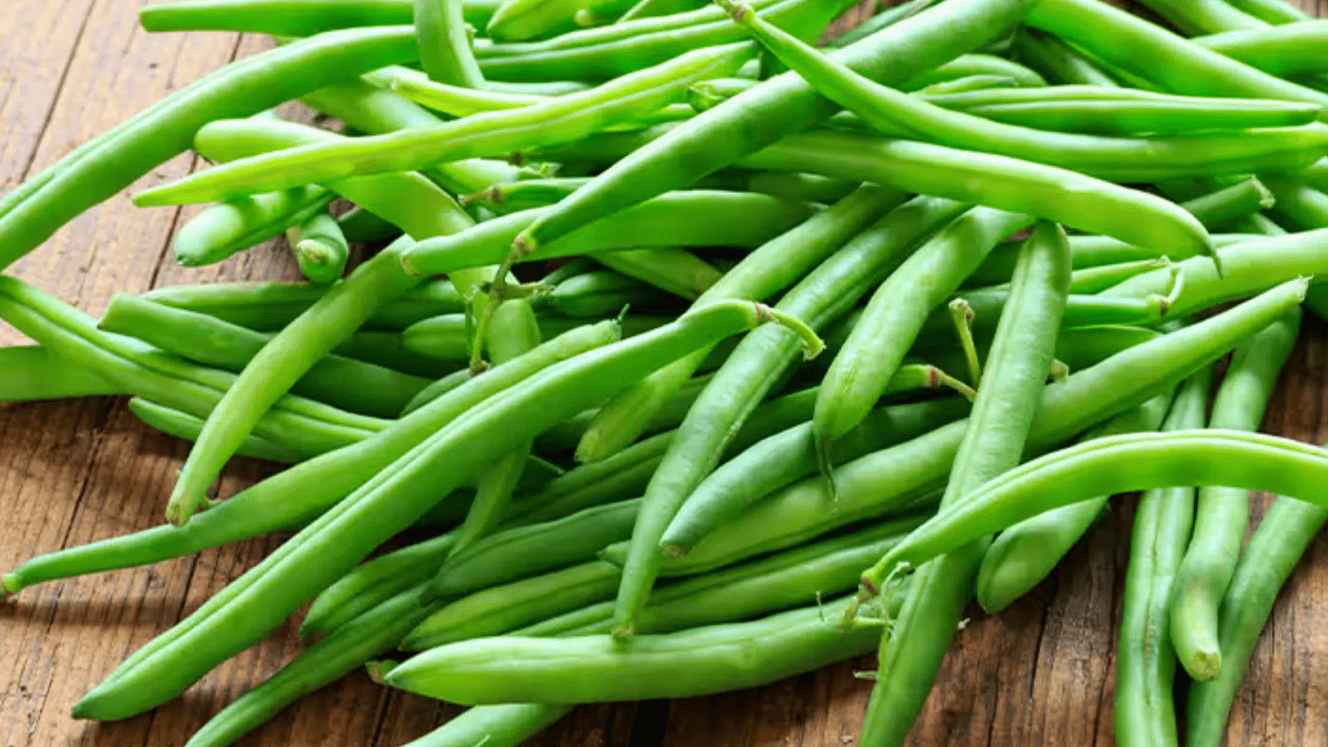 pile of fresh green beans spread across a wooden surface, showing their long shape and bright green color