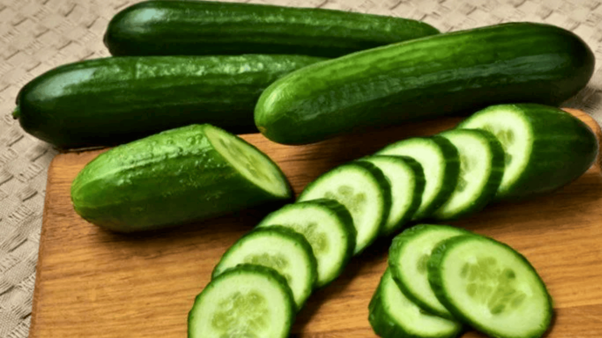 whole cucumbers and fresh cucumber slices arranged on a wooden cutting board, showing crisp green skin and pale interior