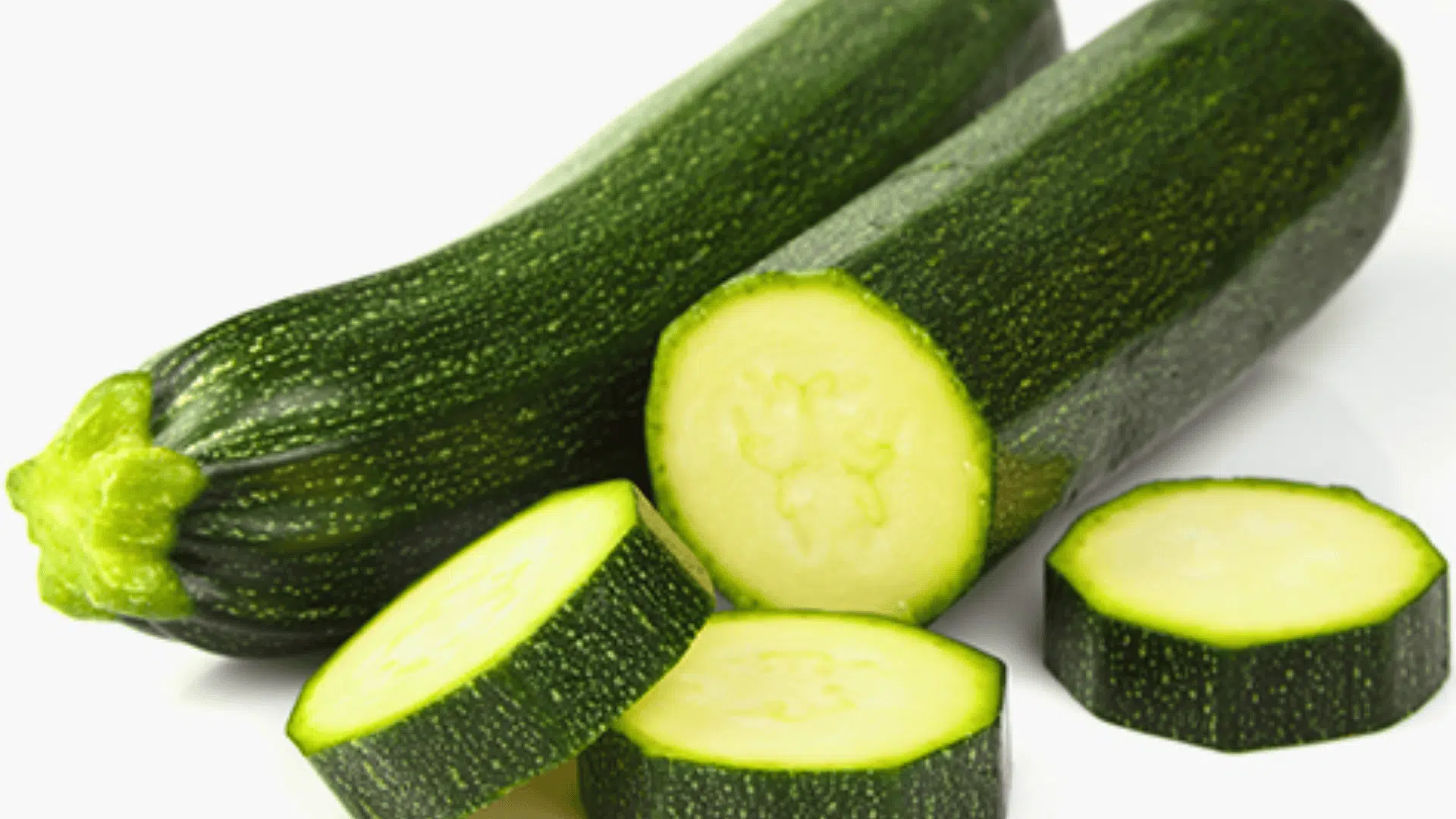 whole zucchini with several round slices cut in front, showing the pale interior and dark green skin