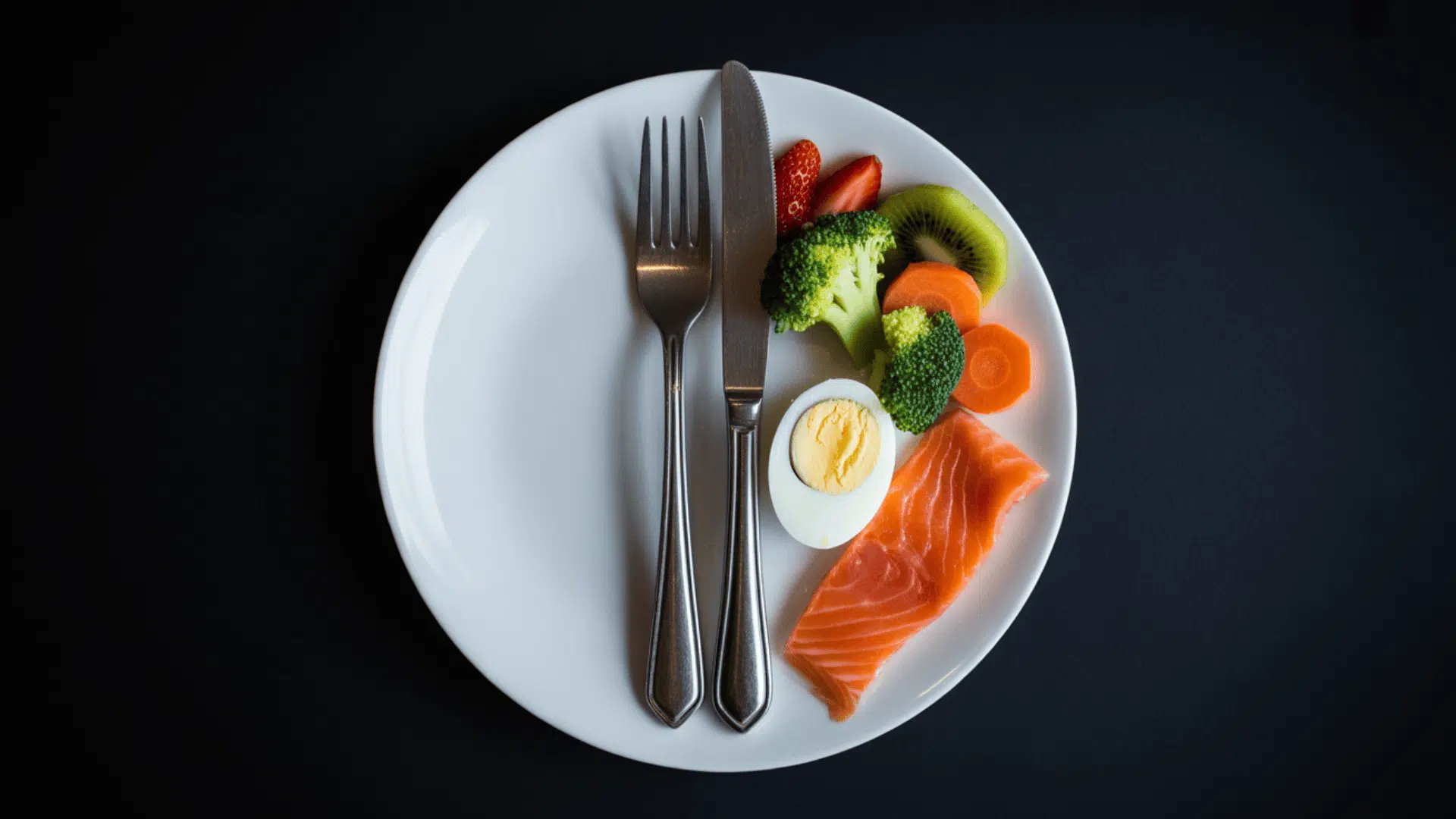 a plate with a fork and knife and small portions of salmon boiled egg broccoli carrot kiwi and strawberry
