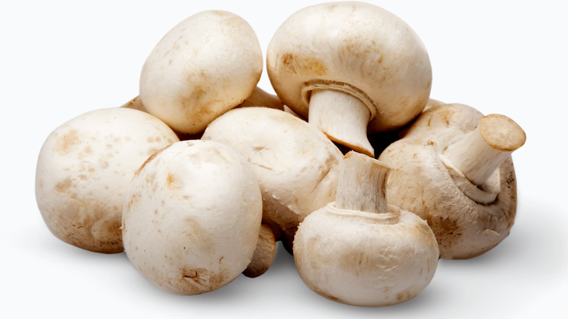 fresh, white button mushrooms with smooth caps and short stems, piled together against a clean white background