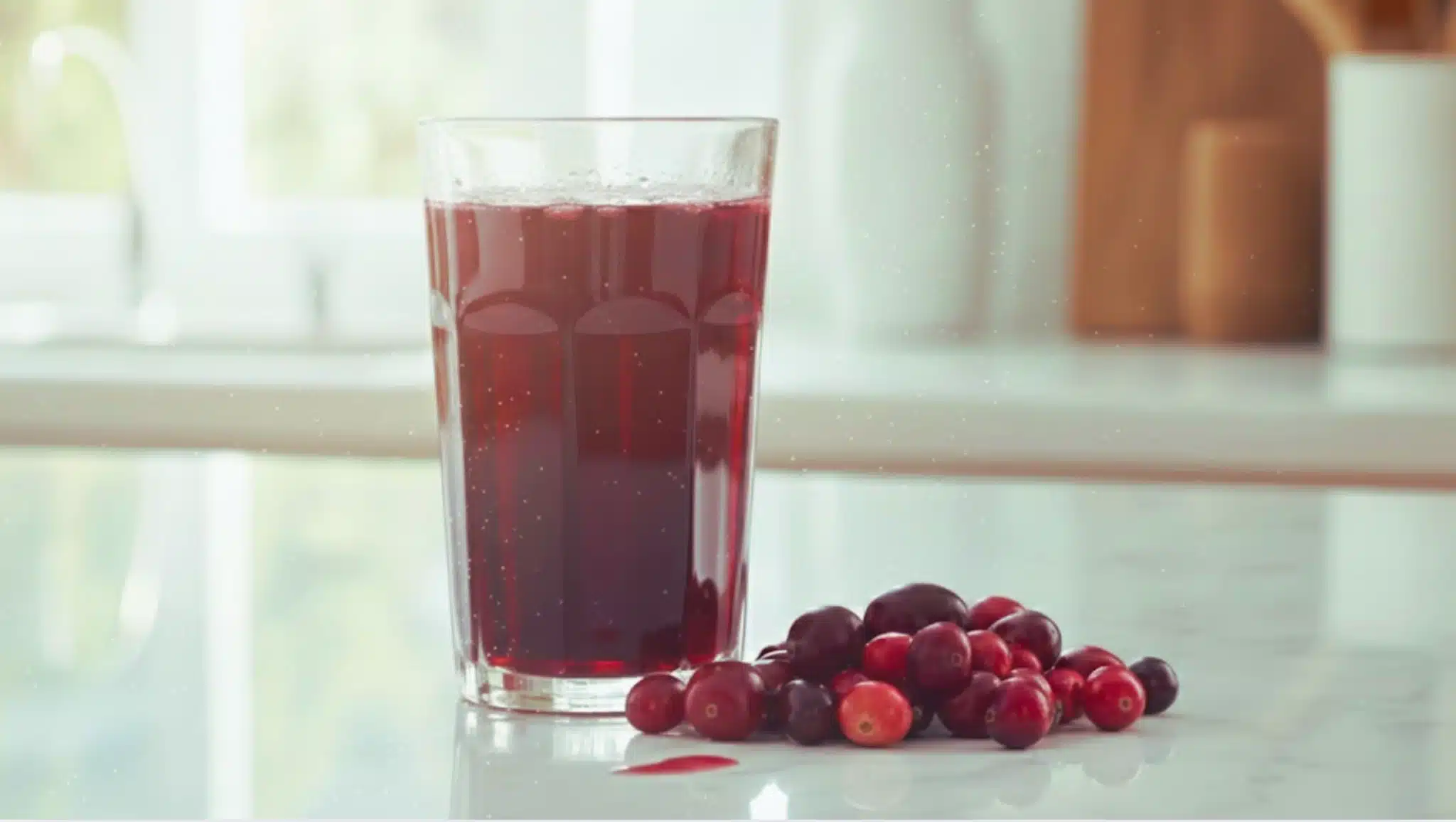 glass of red cranberry juice with fresh cranberries on kitchen countertop in soft natural daylight