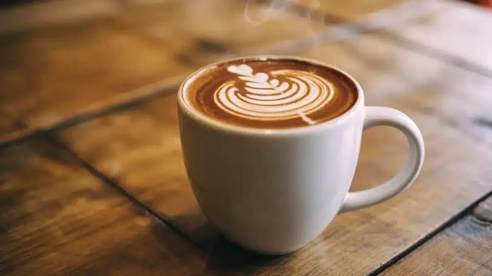 white ceramic latte with spiral milk art on rustic wooden table in warm natural light