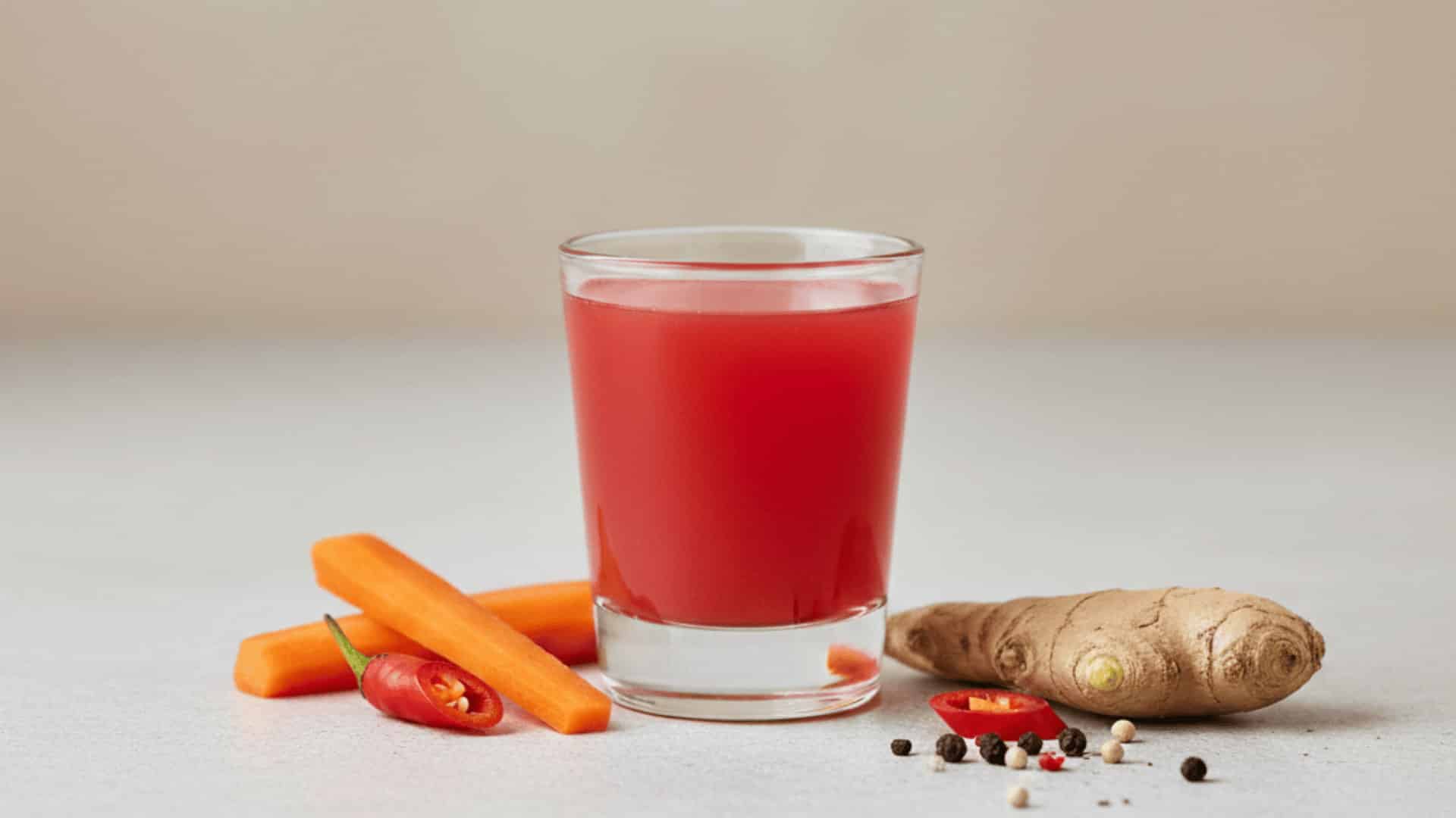 a fiery red metabolism-boosting shot in a glass, with fresh carrots, ginger, and chili pepper on a minimal background