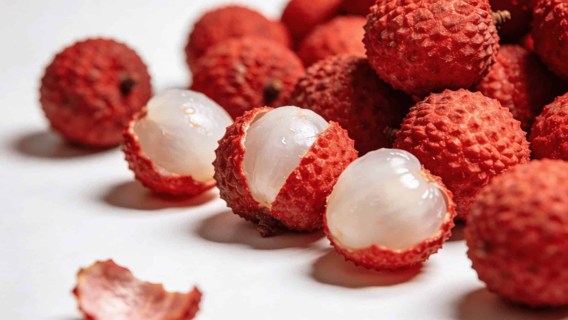 a pile of fresh lychee fruits with a few peeled showing white flesh on a clean white surface