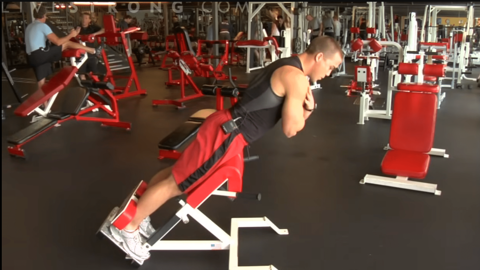 an athlete in a gym performing back extensions on a red hyperextension bench to strengthen his lower back and core
