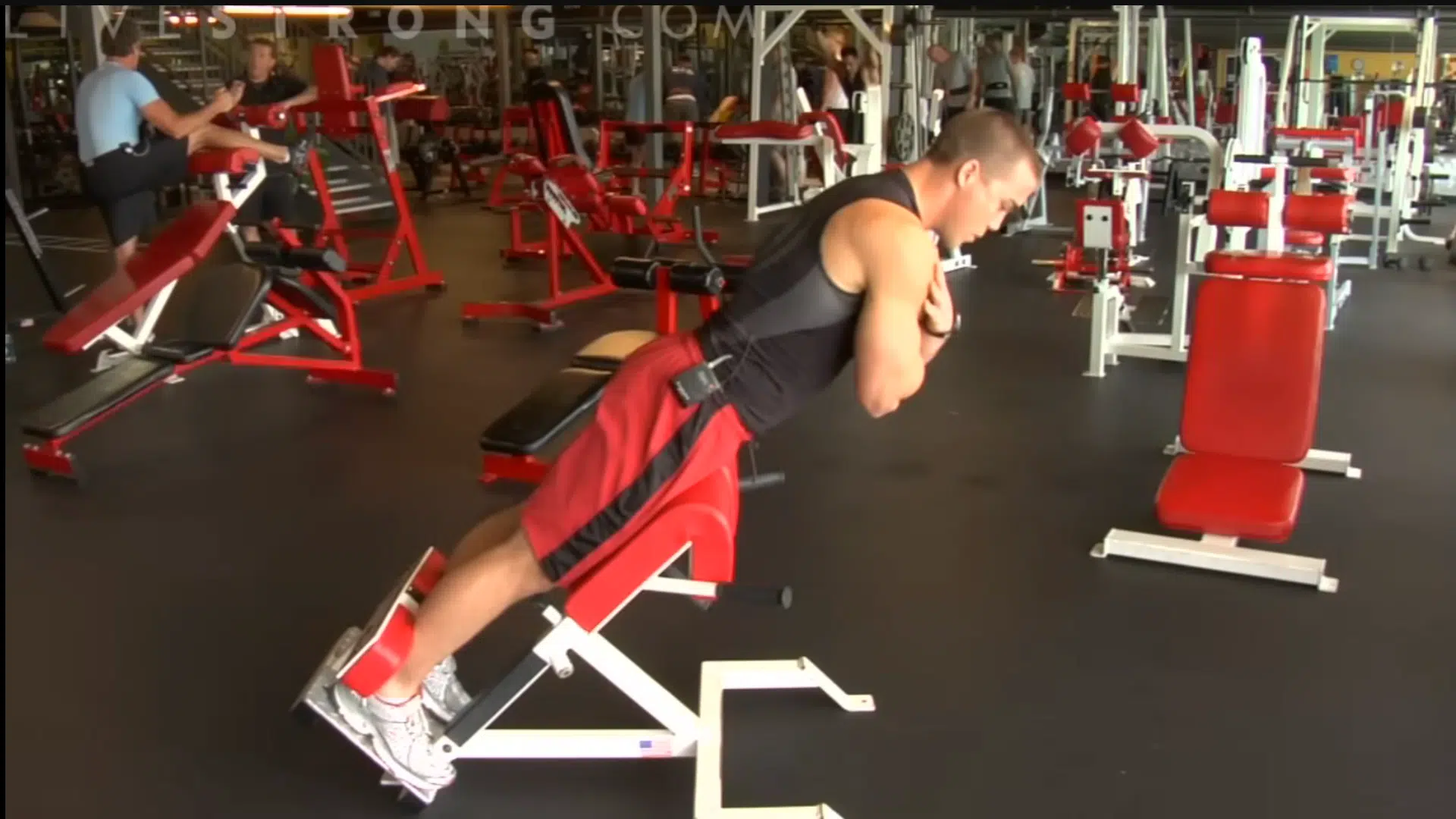 an athlete in a gym performing back extensions on a red hyperextension bench to strengthen his lower back and core
