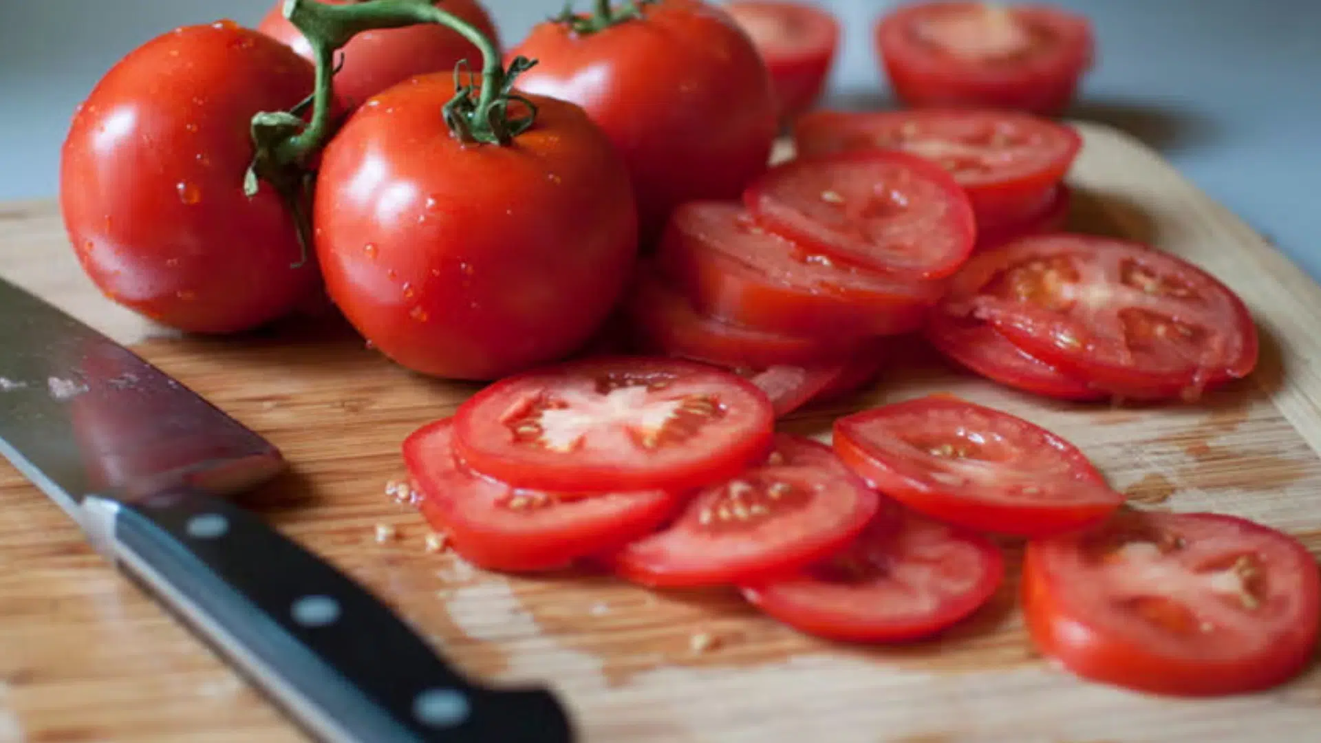 assorted whole and sliced tomatoes, including cherry and grape varieties, arranged on a wooden board with fresh basil and parsley