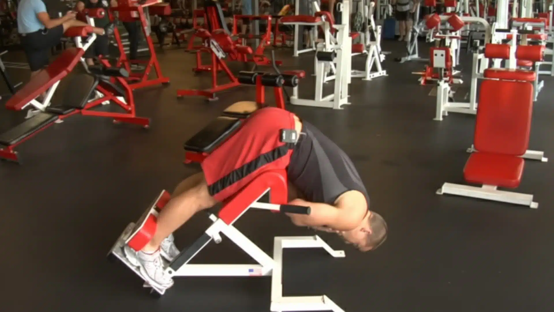 athlete in a gym performing back extensions on a red hyperextension bench to strengthen his lower back and core