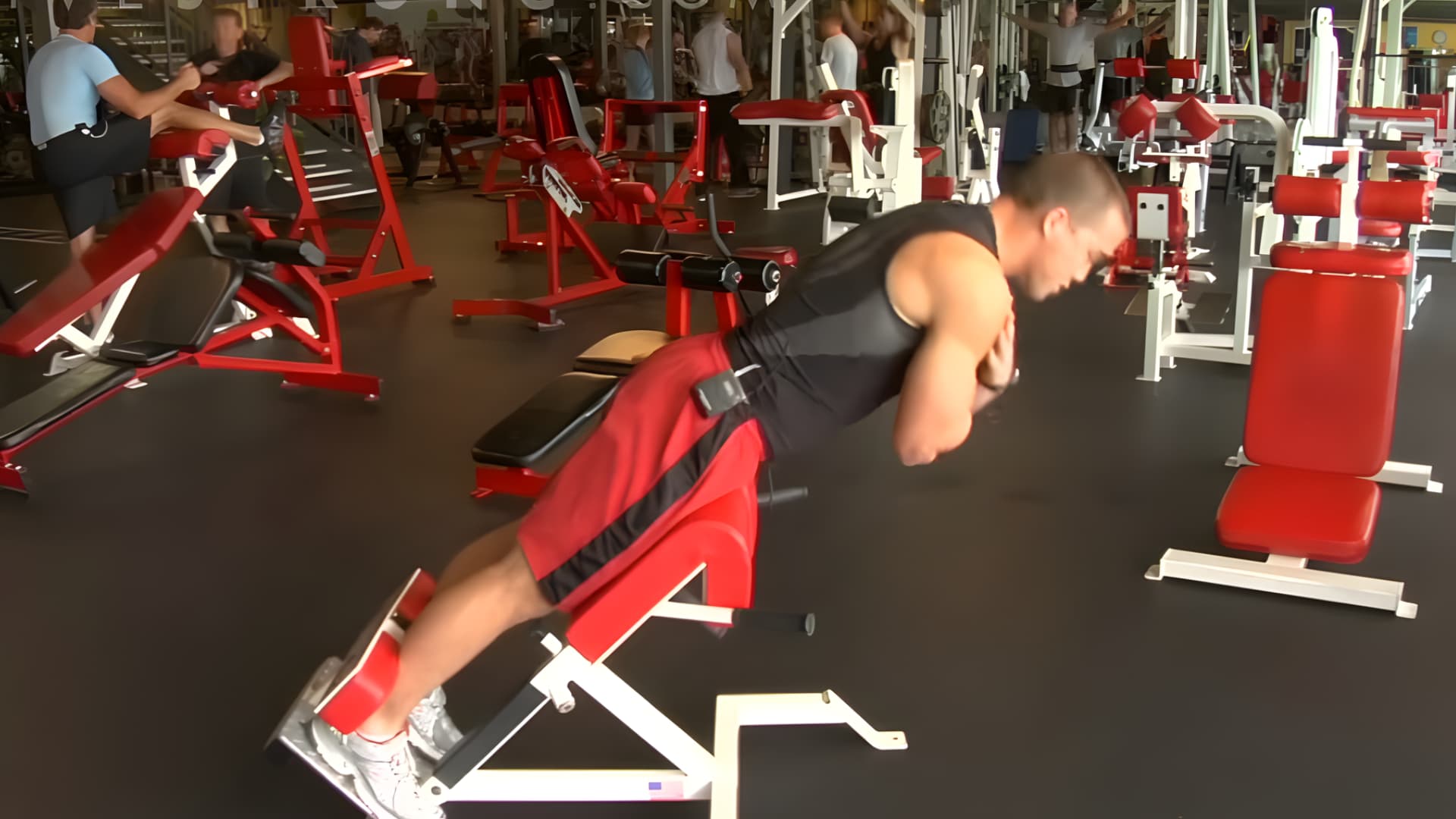 athlete in a gym performing back extensions on a red hyperextension bench to strengthen his lower back and core