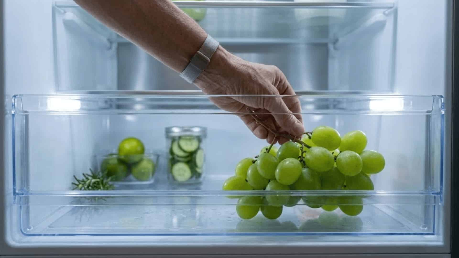 bunch of fresh green grapes being placed inside a clean open refrigerator drawer with soft cool lighting