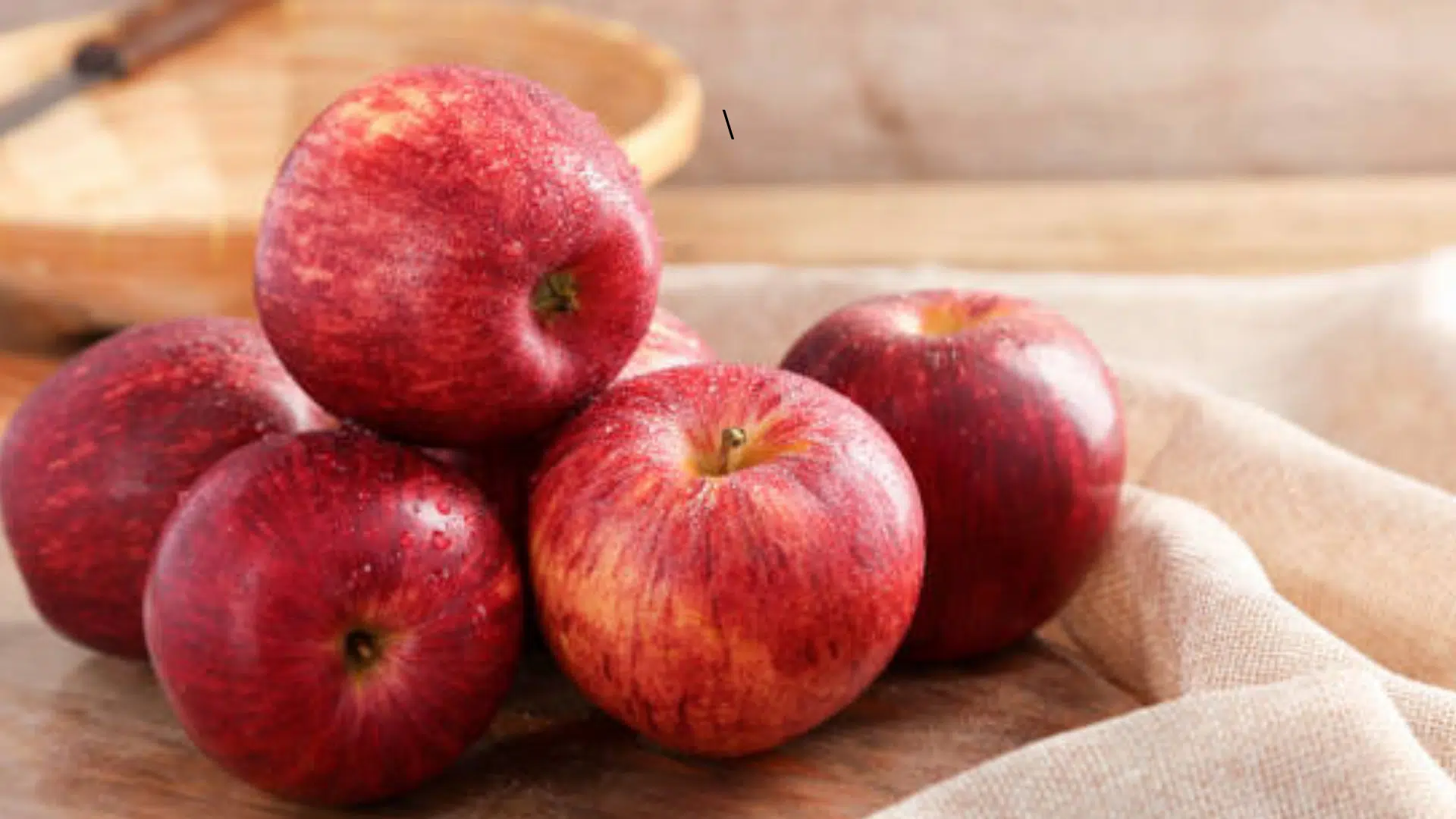 fresh Gala apples from Iran piled in a round woven basket on a wooden table in a sunlit kitchen setting