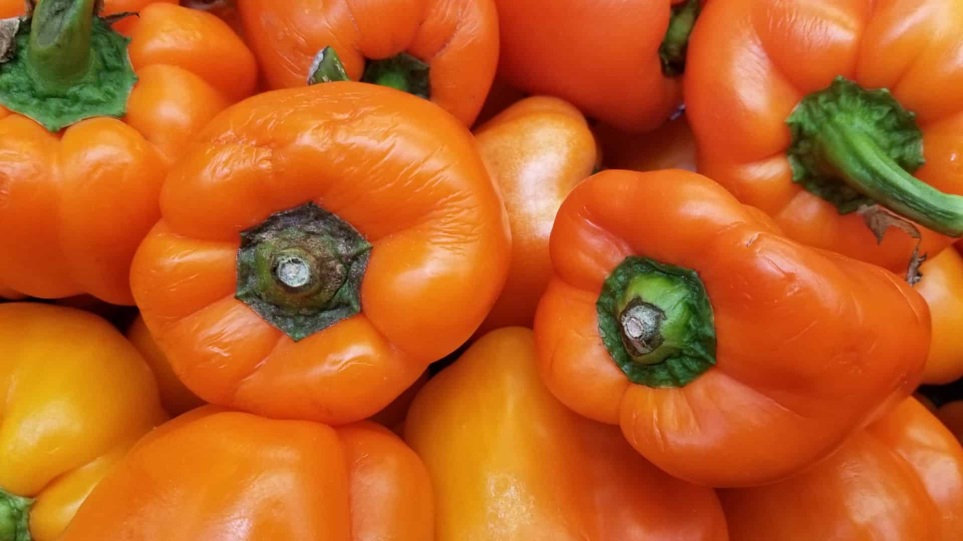 image of multiple fresh orange bell peppers, showcasing their vibrant color and green stems, piled together