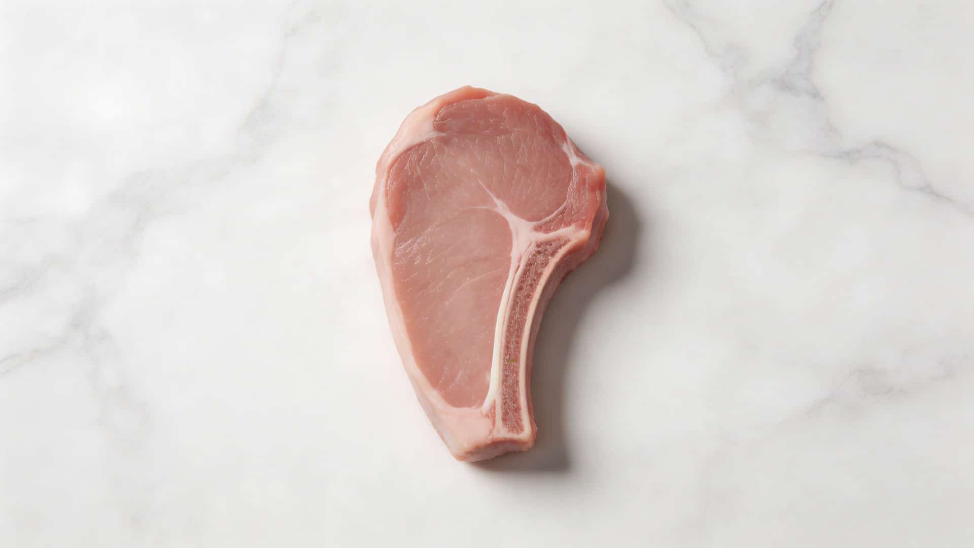 lean center-cut pork chop with minimal fat on white marble surface, clean trim, overhead food photography view