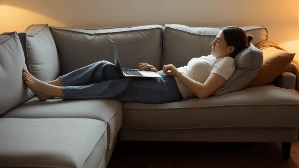 person slouching on couch while using laptop with legs stretched out showing poor posture that can strain the lower back