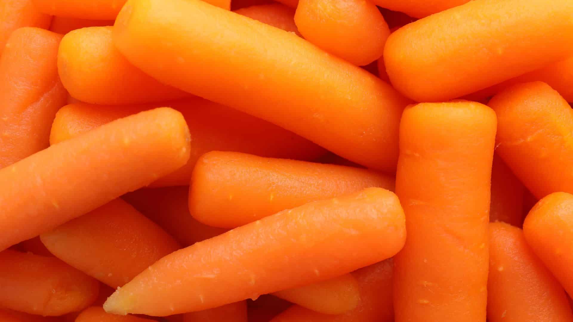 pile of vibrant, peeled baby carrots creates a bright orange background, showcasing their smooth texture and rounded, uniform shapes