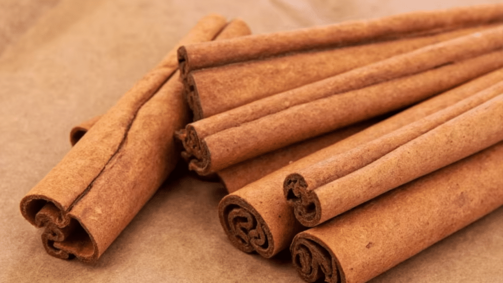 several brown cinnamon sticks bundled together on a neutral, textured surface, showcasing their natural, curled bark layers
