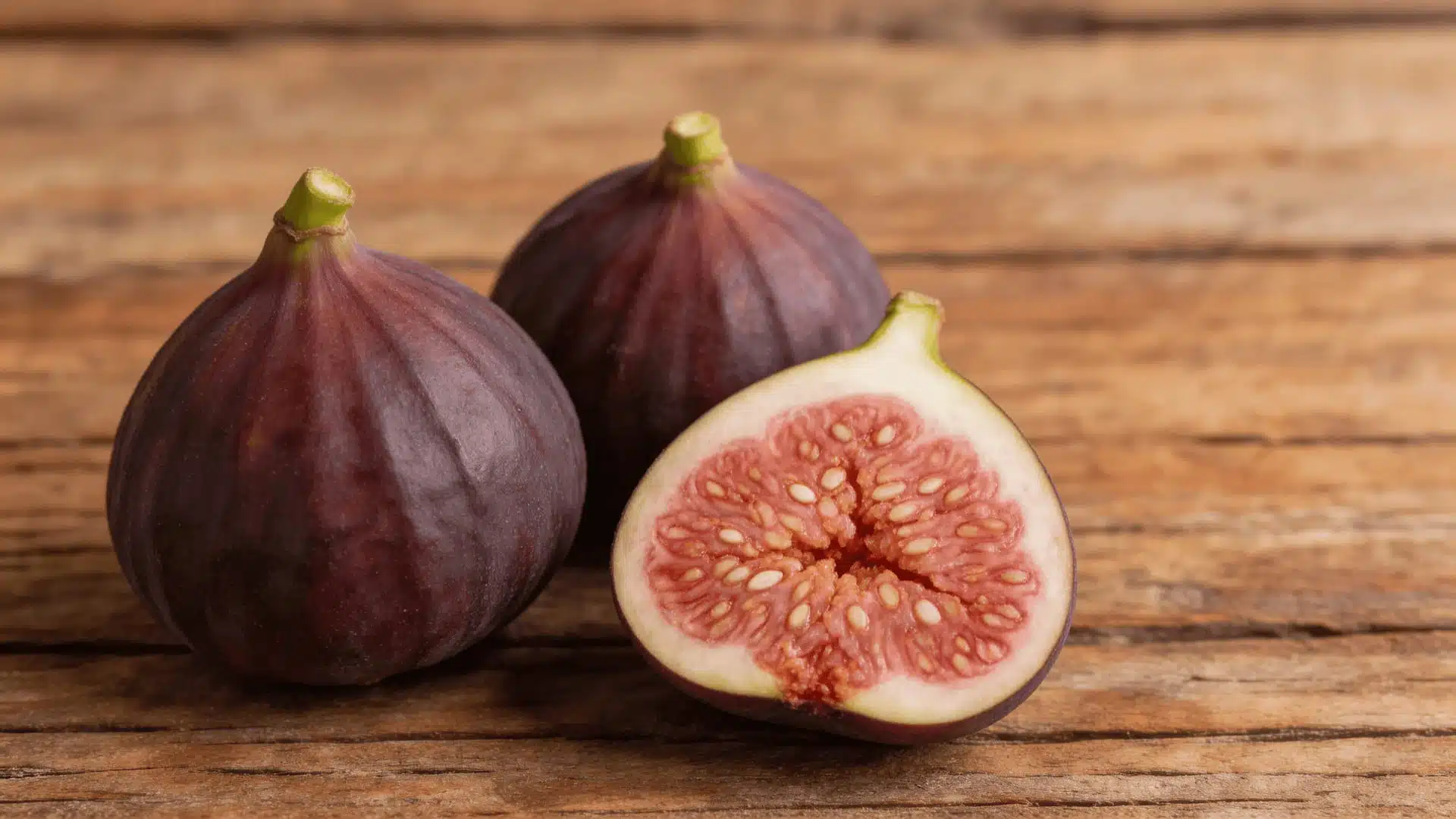 three fresh figs with one sliced open showing pink flesh arranged on a rustic wooden surface
