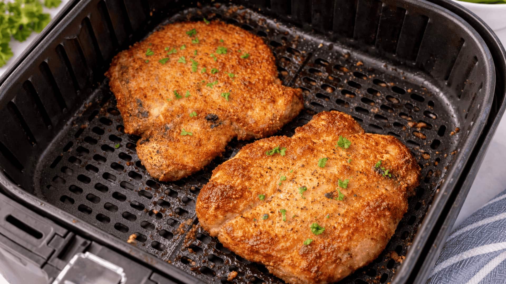 two golden-brown air fryer pork chops garnished with parsley, placed in an air fryer basket