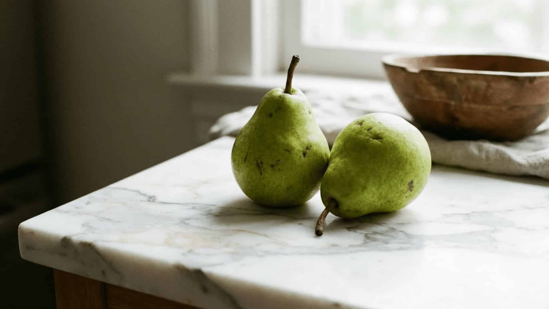 two ripe green pears sitting on a light marble surface under soft diffused natural lighting