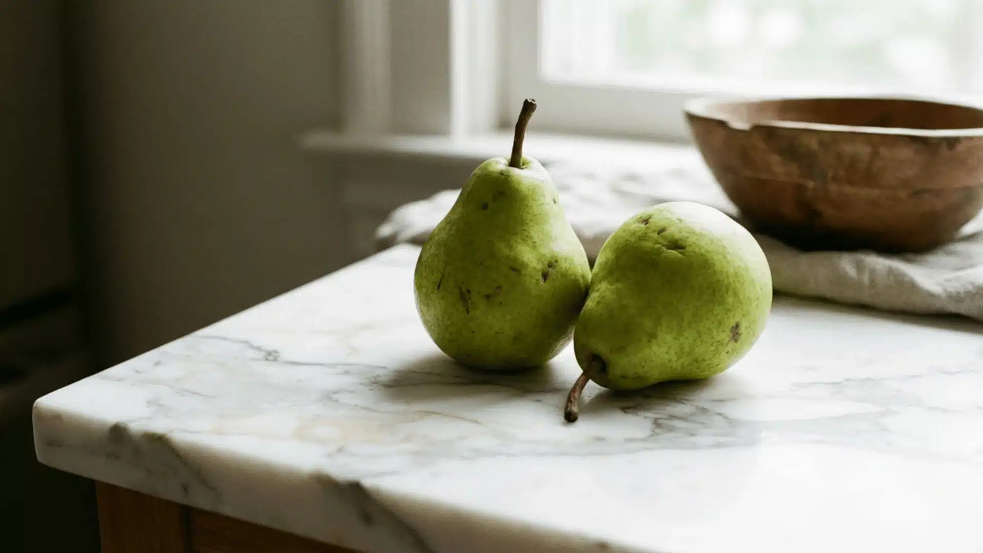 two ripe green pears sitting on a light marble surface under soft diffused natural lighting