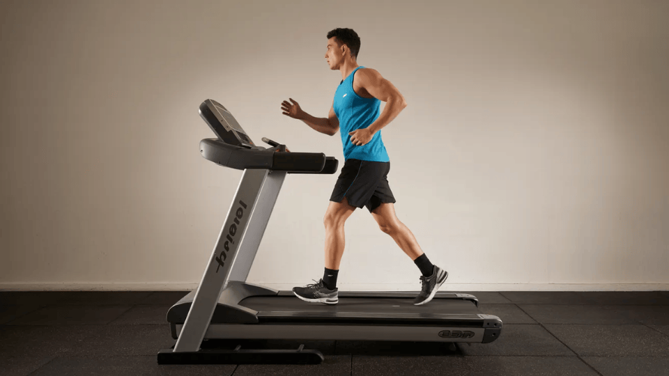 a man in a blue tank top running on a treadmill in a gym setting with a neutral background