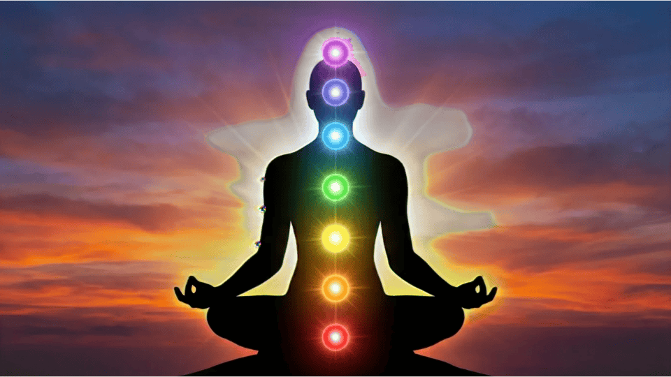 a meditating silhouette with all seven glowing chakra energy points aligned along the spine against a vibrant sunset sky