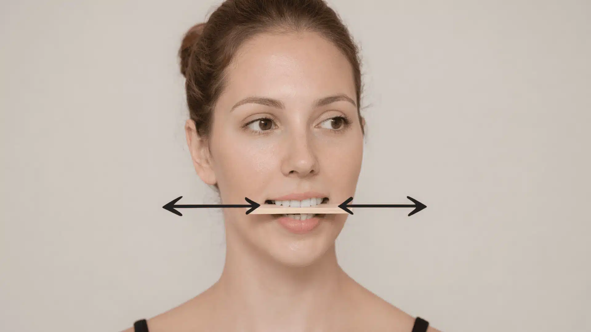 a woman demonstrating a lateral jaw movement exercise with a popsicle stick between her teeth