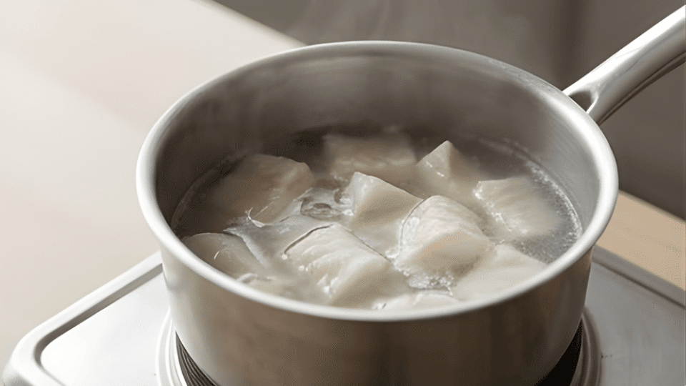 cod pieces cooking in light broth turning opaque in saucepan