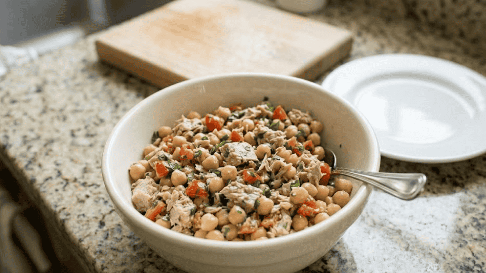 finished salad in a white bowl with a spoon, next to a clean plate on a counter