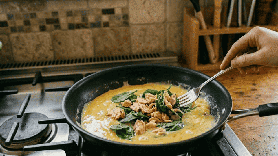 flaked salmon and fresh spinach are added to the warm scrambled eggs in the pan