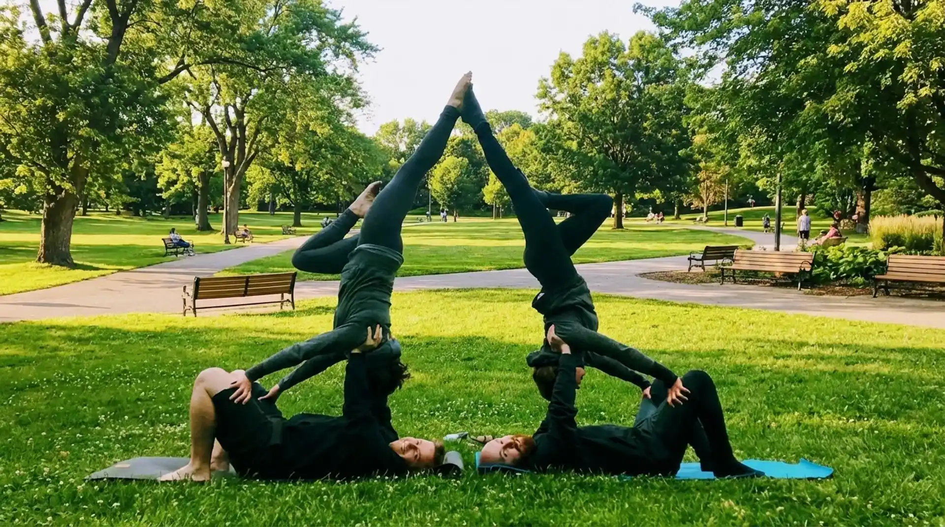 four people performing advanced acro yoga pyramid pose in park, balancing inverted positions with strong core control