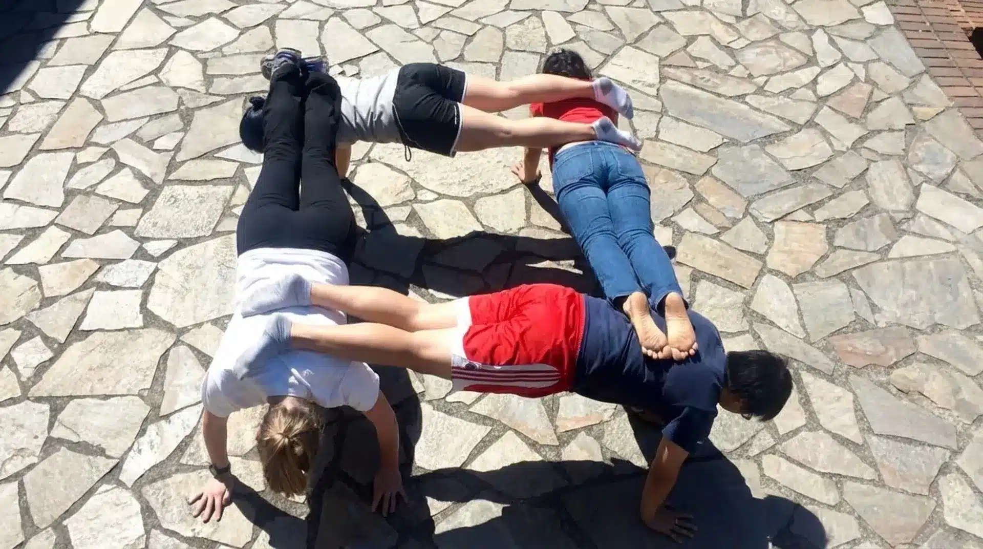 four people performing group plank yoga pose outdoors, balancing body weight with strong core engagement and teamwork