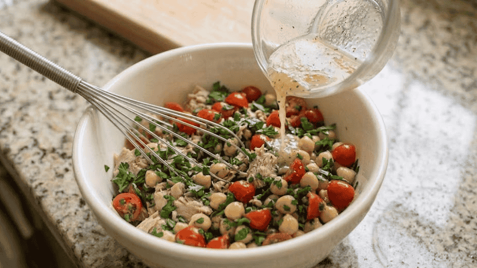 lemon and black pepper dressing poured from a glass cup over the salad with a whisk