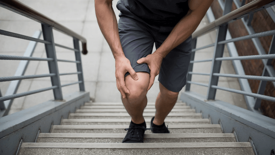 man holding his knee in pain while climbing stairs wearing grey shorts and black sneakers