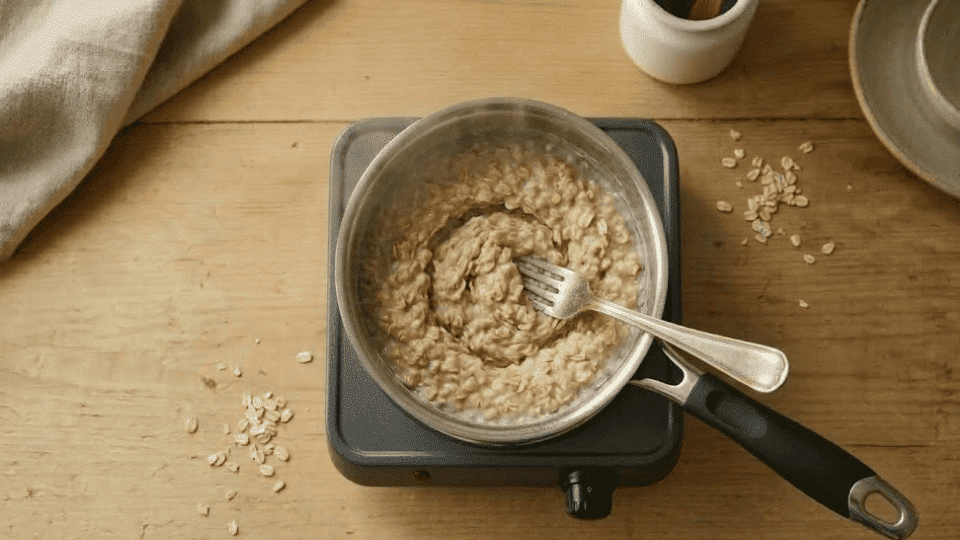 quick oats cooking in a saucepan and being stirred with a spoon on a light wooden kitchen counter