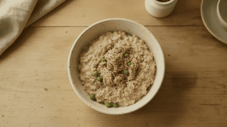 savory tuna oatmeal bowl with peas and black pepper served warm on a light wooden kitchen counter