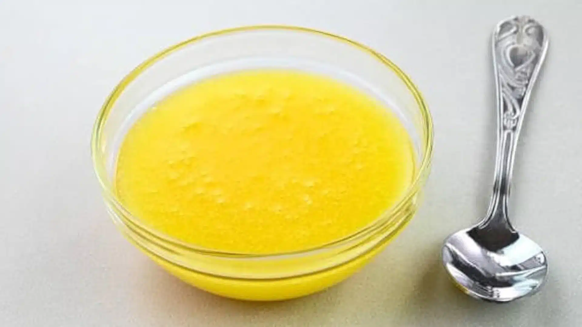 small glass bowl filled with vibrant yellow melted ghee or clarified butter sits next to a silver ornate spoon