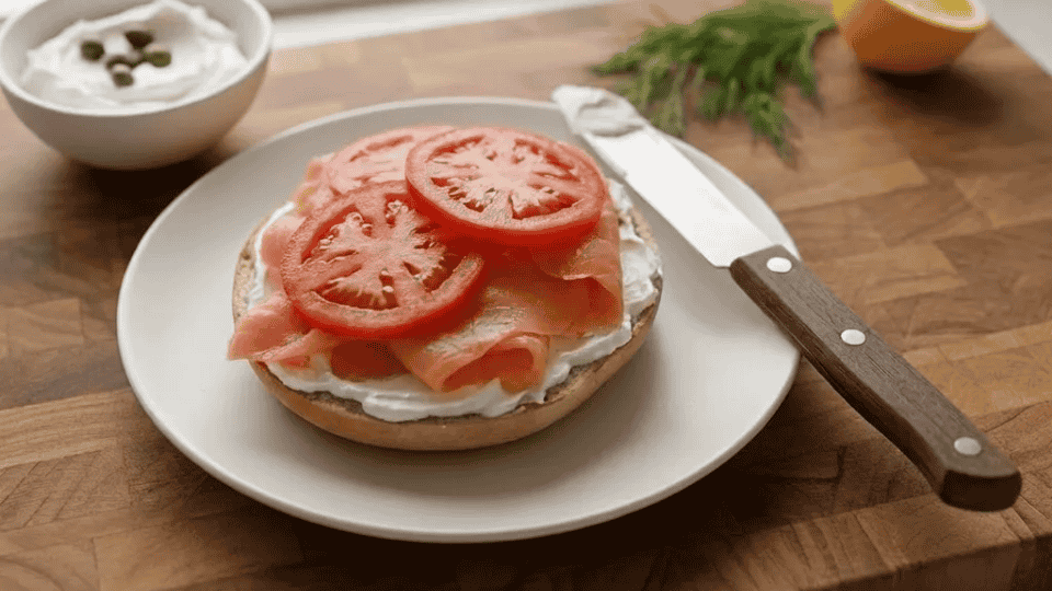 smoked salmon bagel halves on a plate topped with fresh tomato slices