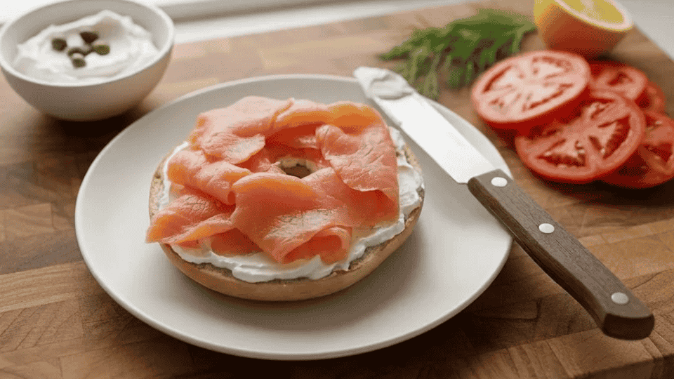 toasted bagel halves on a plate topped with folded, delicate slices of pink smoked salmon