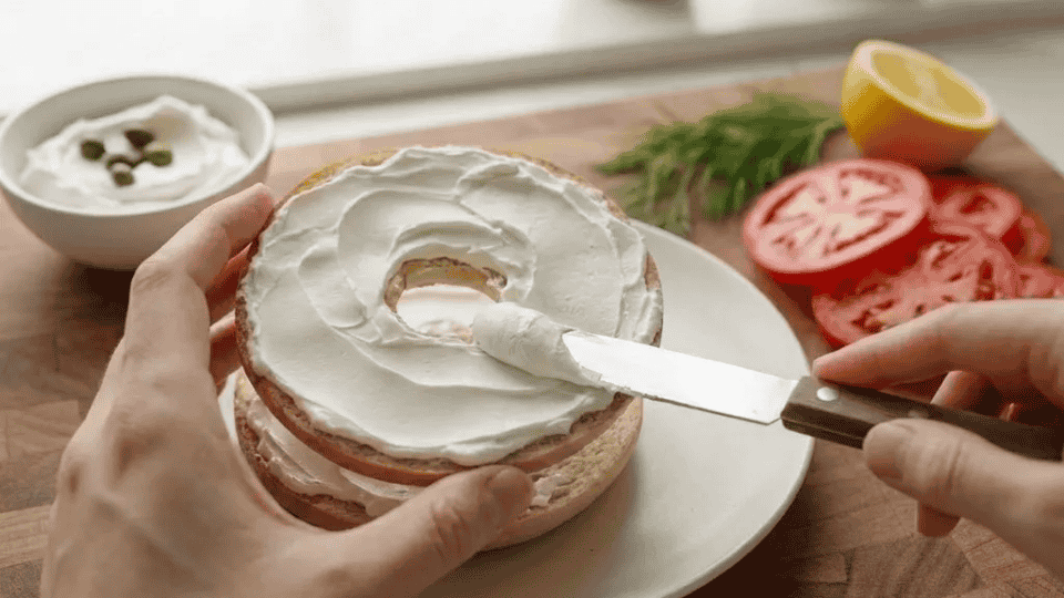 toasted bagel thin halves on a white plate spread with a smooth, even layer of white cream cheese