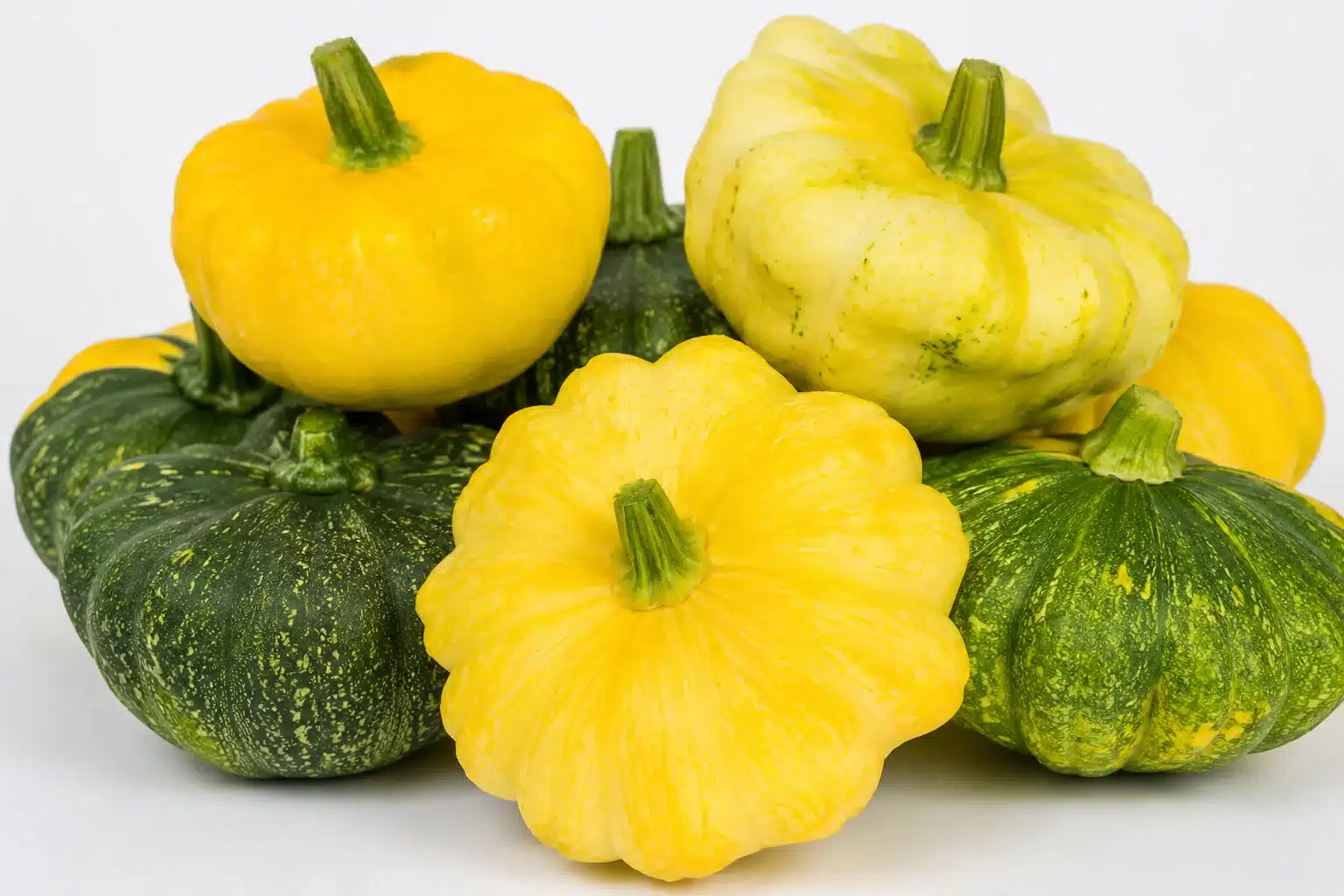 assorted pattypan squash in yellow and green varieties stacked together, showing scalloped shapes,  and short stems