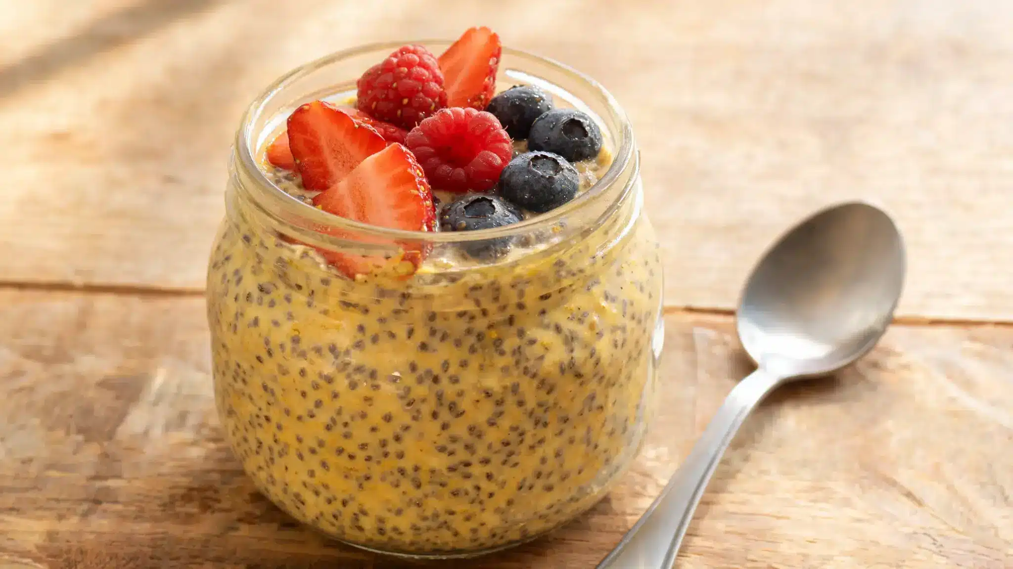 chia pudding with berries and turmeric in a glass jar on a wooden surface
