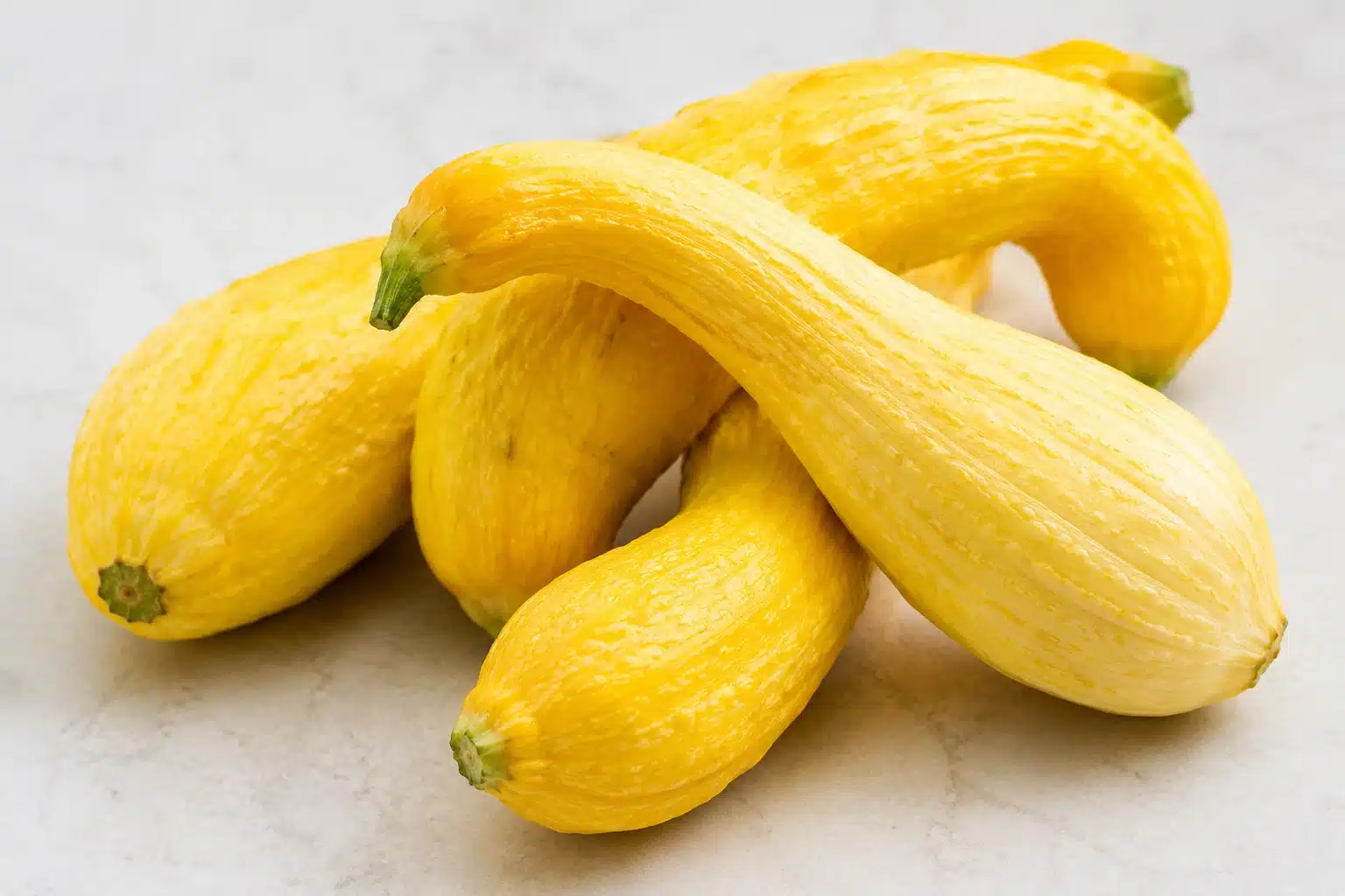 curved yellow squash with textured skin arranged together on light surface, showing varied shapes, and tapered ends