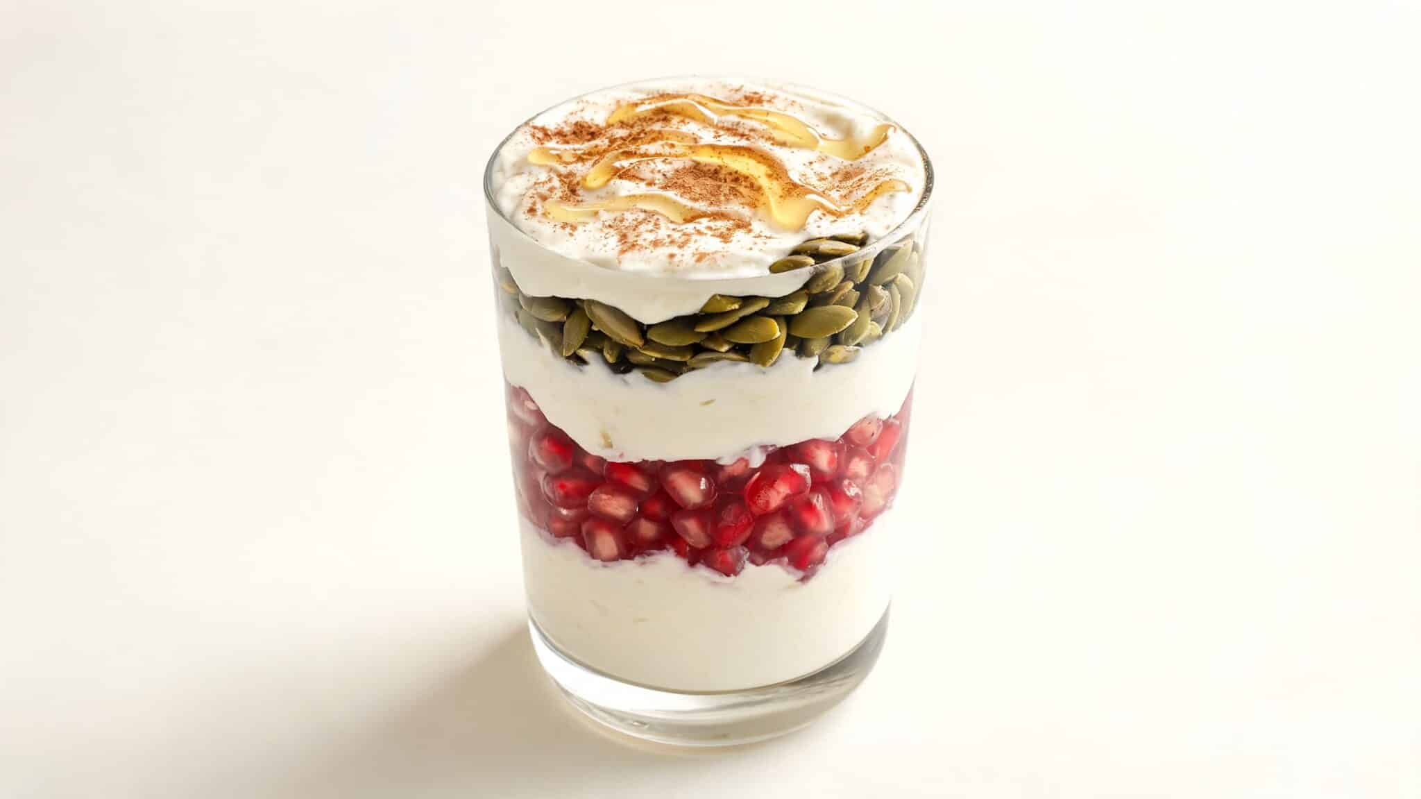 greek yogurt parfait with pomegranate seeds and pumpkin seeds in a clear glass