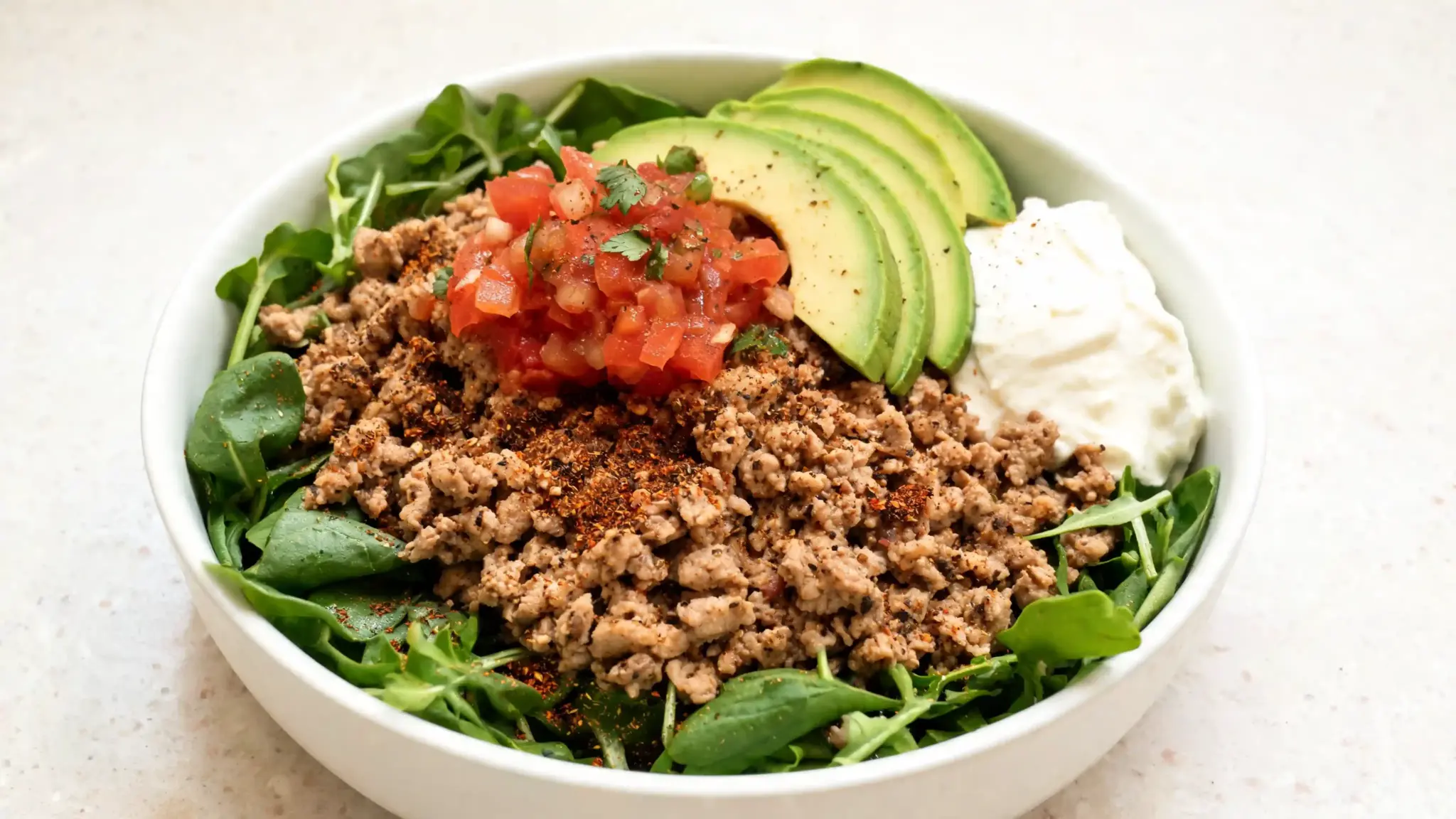ground turkey over greens with avocado, Greek yogurt, and salsa in a healthy taco bowl