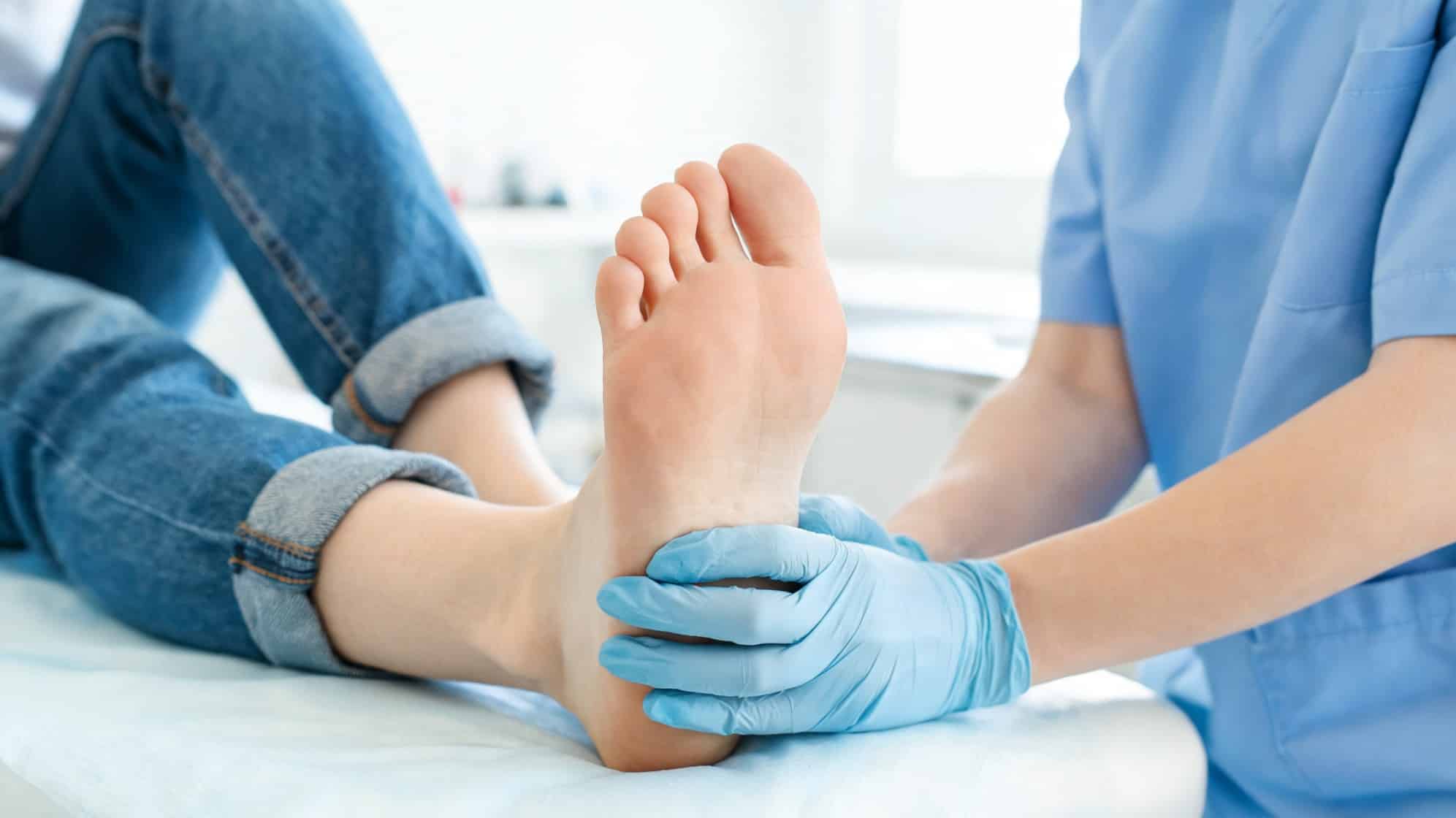 Healthcare professional in blue scrubs gently holds a patient's foot, wearing blue gloves.