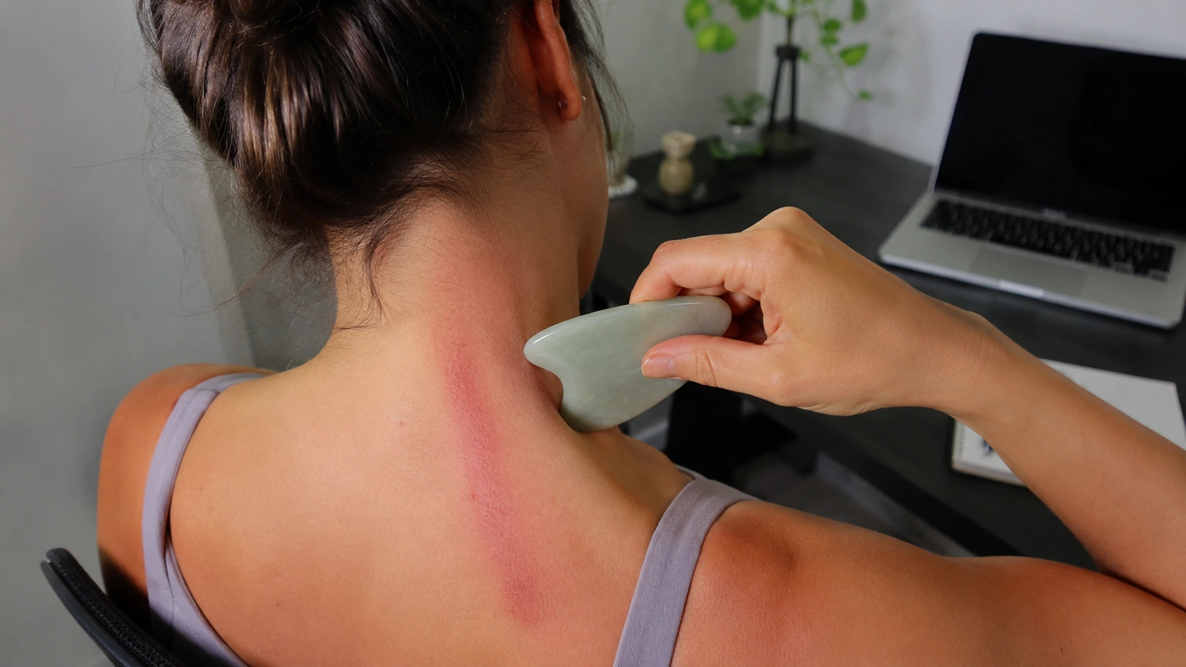 person uses a gua sha tool on the neck and upper back, showing redness from scraping during at-home muscle relief