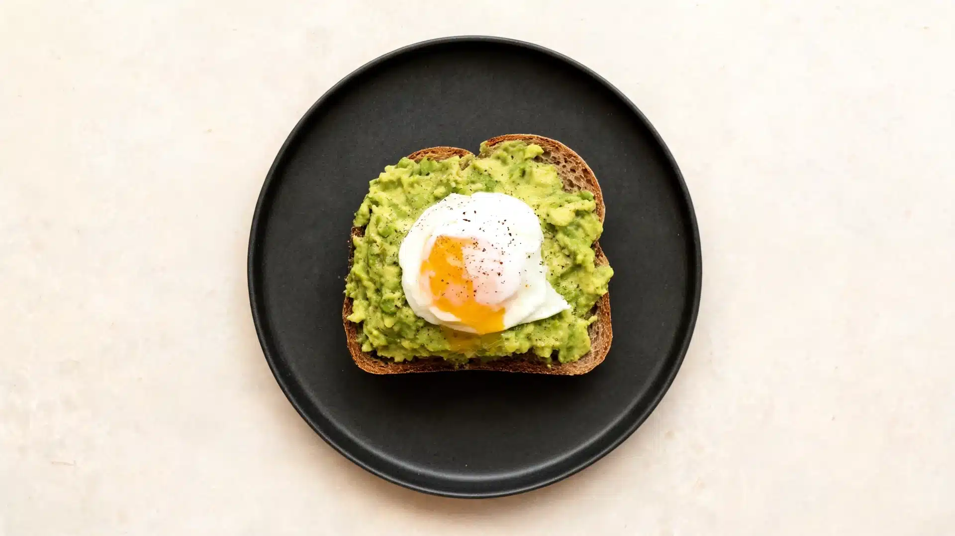 top view of avocado toast with poached egg on a black plate against a light background, simple, minimal breakfast