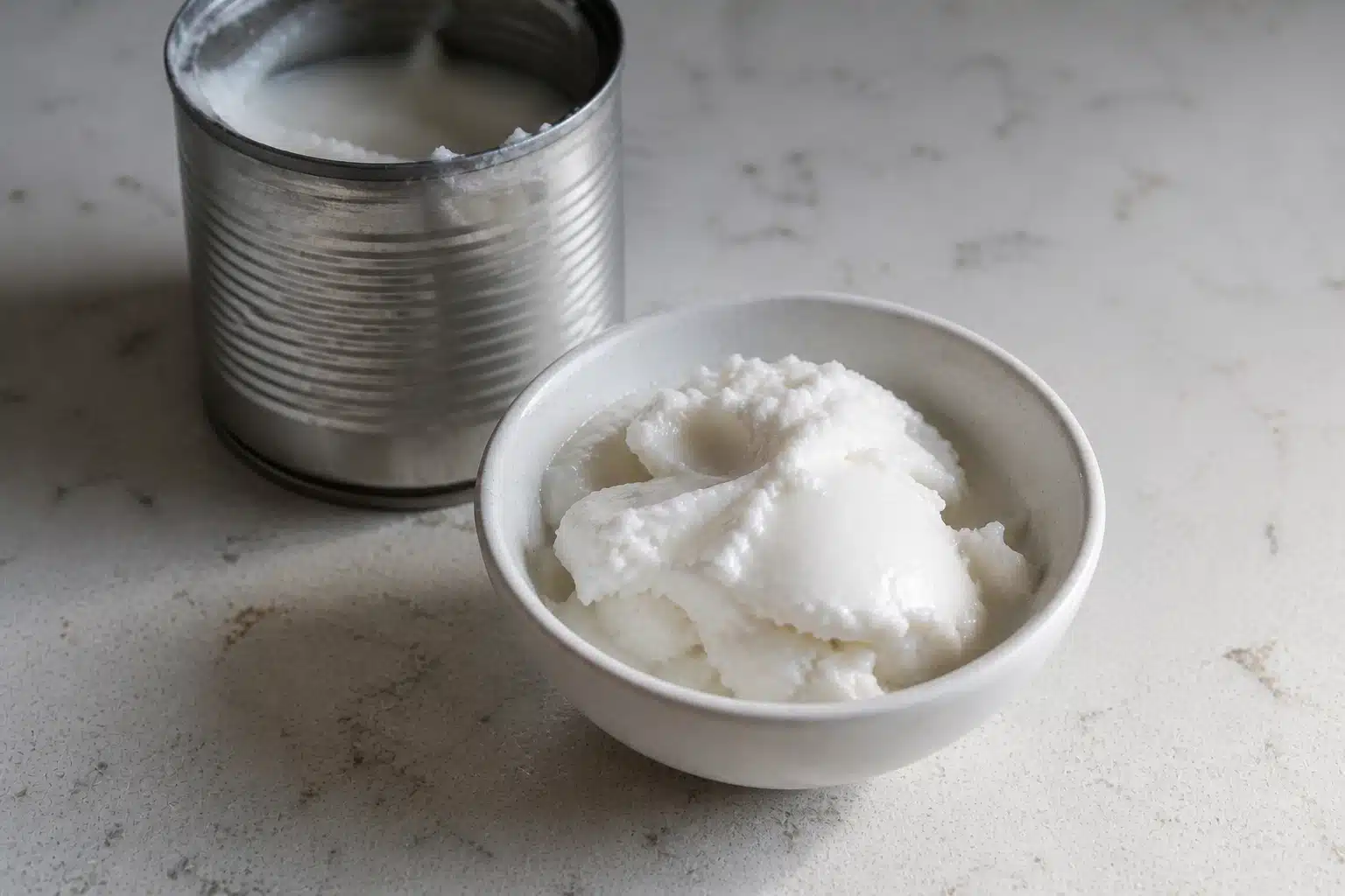 white bowl with thick coconut cream on marble counter, open can behind slightly blurred, soft natural daylight